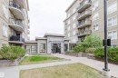 Modern building exterior featuring a stone facade entrance, multi-story design, individual balconies with black railings, and mature landscaping with shrubs - 1-405 4245 139 Avenue, Edmonton, AB 
