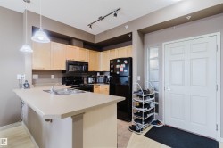 Kitchen featuring light wood cabinetry, black appliances, track lighting, and a peninsula with an integrated sink - 