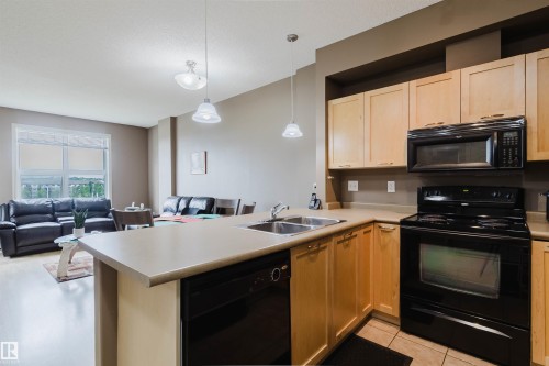 Kitchen featuring light wood cabinetry, black appliances, and a double basin stainless steel sink - 1-405 4245 139 Avenue, Edmonton, AB 