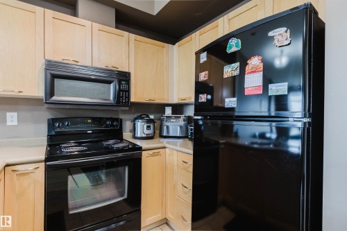 Kitchen featuring light wood-finish cabinetry, black appliances, and neutral countertops - 1-405 4245 139 Avenue, Edmonton, AB 