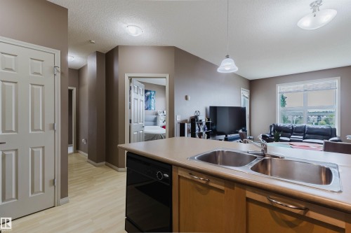 Kitchen featuring a double stainless steel sink, light wood-finish cabinetry, and a black dishwasher - 1-405 4245 139 Avenue, Edmonton, AB 