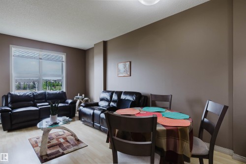 Open-concept living and dining area featuring light wood-finish flooring, neutral wall tones, and a large window providing ample natural light - 1-405 4245 139 Avenue, Edmonton, AB 
