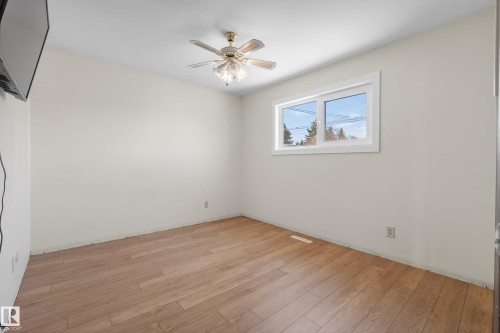 Bright room featuring wood-finish flooring, a white-framed window, a ceiling fan with integrated lighting, and neutral wall tones - 6203 90 Avenue, Edmonton, AB 