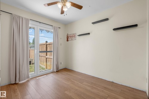 Wood-finish flooring throughout, featuring a ceiling fan with integrated lighting, and white patio doors providing exterior access - 6203 90 Avenue, Edmonton, AB 