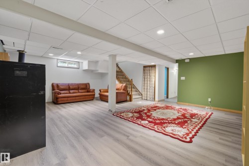 Spacious room featuring light wood-finish flooring, a drop ceiling with recessed lighting, and a partial accent wall in a deep green hue - 6203 90 Avenue, Edmonton, AB 