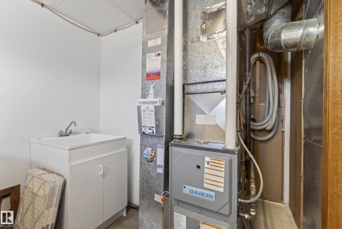 Utility area featuring a white utility sink with a chrome faucet, white base cabinetry, and a Daikin HVAC system with exposed ductwork - 6203 90 Avenue, Edmonton, AB 