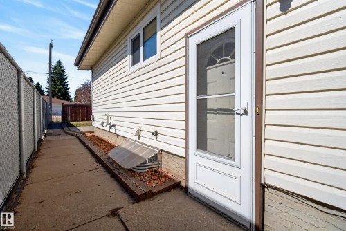 Side exterior entry with a white storm door, beige horizontal siding, and a concrete pathway - 6203 90 Avenue, Edmonton, AB 