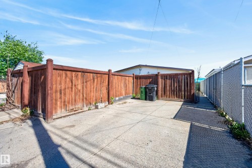 Paved concrete area featuring a natural wood privacy fence and chain-link fencing - 6203 90 Avenue, Edmonton, AB 