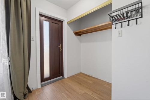 Entryway featuring wood-finish flooring, a wood-panel door with privacy glass, white trim, and a built-in storage shelf with a hanging rod - 6203 90 Avenue, Edmonton, AB 