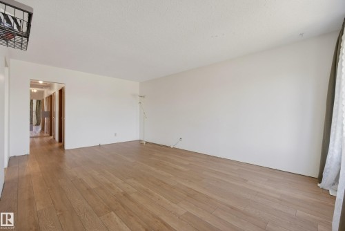 Expansive room featuring wood-finish flooring, light-toned wall finishes, and a textured ceiling - 6203 90 Avenue, Edmonton, AB 