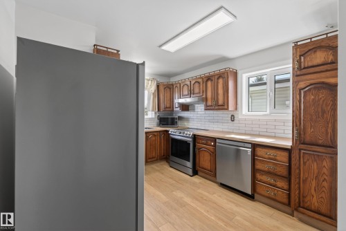 Kitchen featuring wood-finish cabinetry, stainless steel appliances, and wood-finish flooring - 6203 90 Avenue, Edmonton, AB 