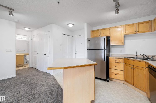 Kitchen with wood-finish cabinetry, stainless steel refrigerator, and integrated sink - 320 245 Edwards Drive, Edmonton, AB 