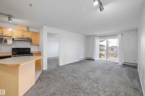 Open-concept living space with light wood cabinetry and a kitchen island - 320 245 Edwards Drive, Edmonton, AB 