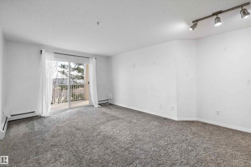 Spacious room featuring neutral carpeting, white walls, and a sliding glass door leading to a balcony - 320 245 Edwards Drive, Edmonton, AB 