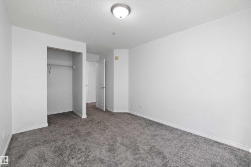 Spacious room featuring neutral grey carpeting, white walls, and a built-in closet with shelving - 320 245 Edwards Drive, Edmonton, AB 