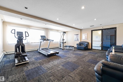 Fitness area featuring patterned carpet flooring, multiple windows with blinds, recessed lighting, and a glass-paneled entry door - 320 245 Edwards Drive, Edmonton, AB 