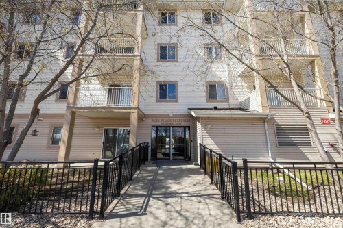 Multi-story building featuring light-colored siding, multiple balconies with white railings, and a ground-level entrance - 320 245 Edwards Drive, Edmonton, AB 