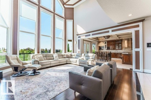 Two-story living area featuring extensive window walls, vaulted ceilings, dark wood-finish flooring, and an open archway to the kitchen - 328 52327 Range Rd 233, Rural Strathcona County, AB 