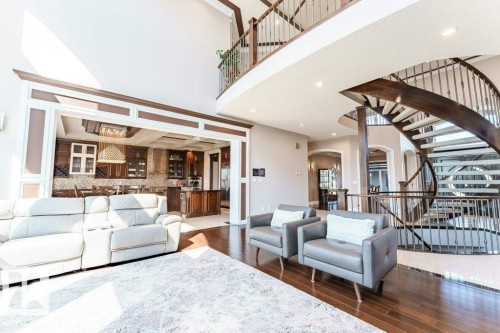 Grand two-story living area featuring a custom spiral staircase with iron balusters, rich wood-finish flooring, and a coffered ceiling in the adjacent kitchen - 328 52327 Range Rd 233, Rural Strathcona County, AB 