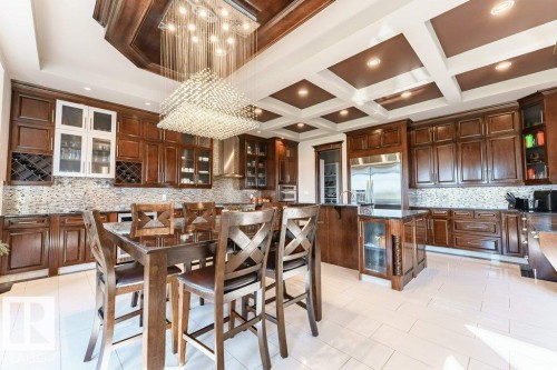 Gourmet kitchen featuring extensive dark wood cabinetry, a large kitchen island with integrated seating, stainless steel appliances, and a coffered ceiling with recessed lighting - 328 52327 Range Rd 233, Rural Strathcona County, AB 