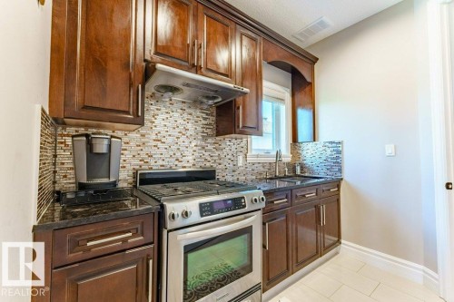 Kitchen featuring rich wood cabinetry, stainless steel oven with gas range, mosaic tile backsplash, dark countertops, and undermount sink with gooseneck faucet - 328 52327 Range Rd 233, Rural Strathcona County, AB 