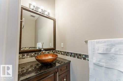 Powder room featuring a vessel sink, dark wood vanity cabinetry, dark countertop, mosaic tile backsplash, and a framed mirror with a four-light vanity fixture - 328 52327 Range Rd 233, Rural Strathcona County, AB 