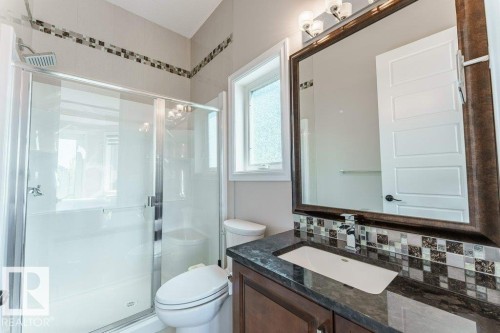 Bathroom featuring a dark wood vanity with an integrated sink, a large framed mirror, and a mosaic tile backsplash - 328 52327 Range Rd 233, Rural Strathcona County, AB 