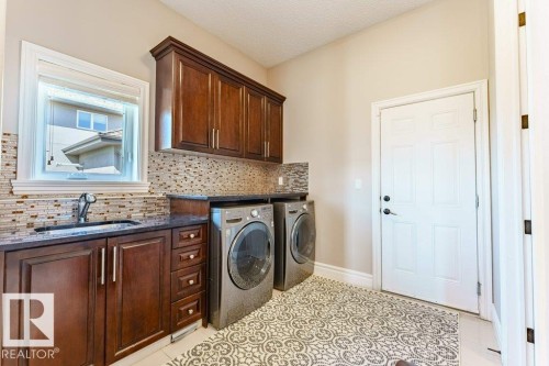 Dedicated laundry room featuring dark wood-finish cabinetry, a sink, and a decorative tile backsplash - 328 52327 Range Rd 233, Rural Strathcona County, AB 
