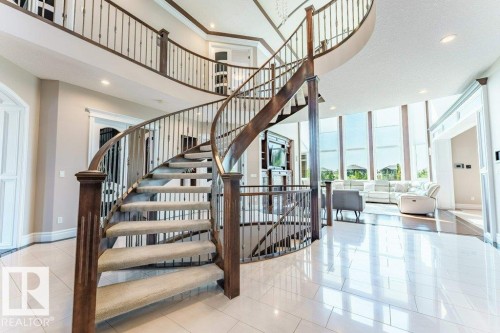 Grand curved staircase featuring wood newel posts, iron balusters, and carpeted treads - 328 52327 Range Rd 233, Rural Strathcona County, AB 