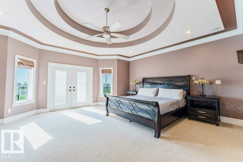 Bedroom featuring a tray ceiling with recessed lighting and a ceiling fan, dual French doors, two windows, and light-colored carpeting - 328 52327 Range Rd 233, Rural Strathcona County, AB 