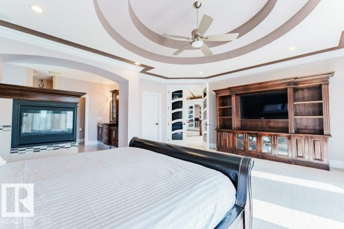 Recessed ceiling with an overhead fan, built-in fireplace with tile surround, wood-finish entertainment center with integrated shelving, arched entryway, and double doors with decorative glass panels - 328 52327 Range Rd 233, Rural Strathcona County, AB 