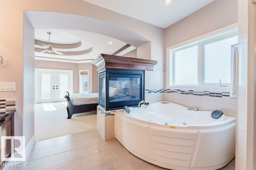 Corner soaking tub with dual windows, a two-sided fireplace, and tiled flooring - 328 52327 Range Rd 233, Rural Strathcona County, AB 