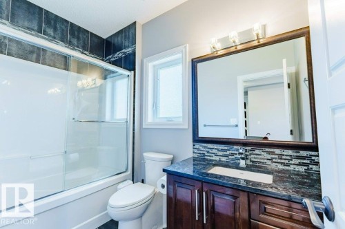 Full bathroom featuring a white tub with sliding glass doors and dark tiled surround - 328 52327 Range Rd 233, Rural Strathcona County, AB 