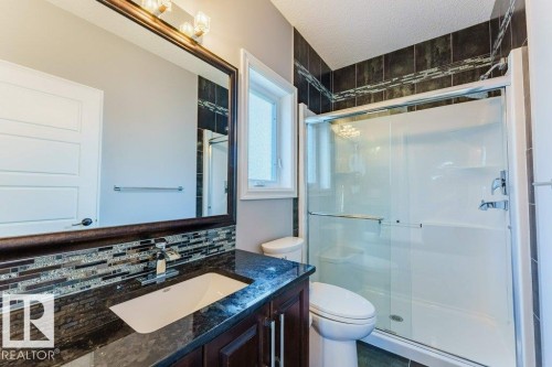 Bathroom featuring a dark wood-finish vanity with an undermount sink, dark granite-style countertop, and a mosaic tile backsplash - 328 52327 Range Rd 233, Rural Strathcona County, AB 