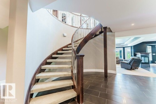 Grand curved staircase with dark wood newel posts and spindles, carpeted treads, and tile flooring - 328 52327 Range Rd 233, Rural Strathcona County, AB 