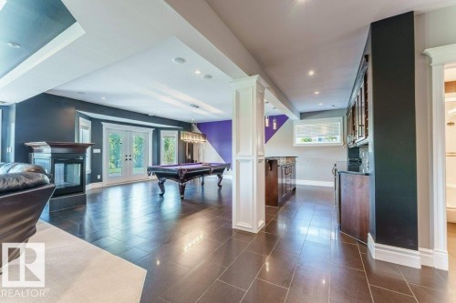 Spacious lower level featuring dark tile flooring, a built-in fireplace, recessed lighting, double glass doors, and a wet bar with cabinetry - 328 52327 Range Rd 233, Rural Strathcona County, AB 
