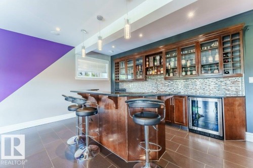 Built-in wet bar featuring dark wood cabinetry, glass-front upper cabinets, a mosaic tile backsplash, and an integrated beverage refrigerator - 328 52327 Range Rd 233, Rural Strathcona County, AB 