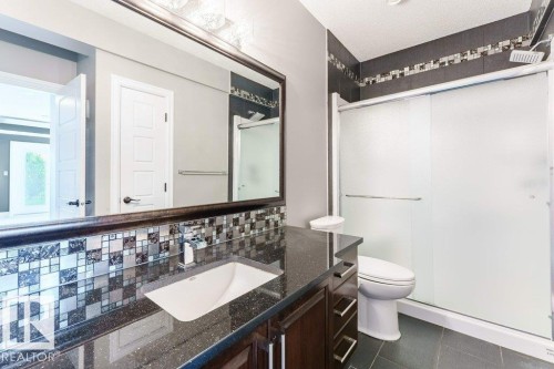 Contemporary bathroom featuring a dark speckled countertop with an undermount sink, a mosaic tile backsplash, and a large mirror - 328 52327 Range Rd 233, Rural Strathcona County, AB 