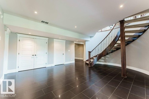 Spacious lower level featuring dark rectangular floor tiles, a curved wood staircase with wrought iron balusters, recessed lighting, and white paneled doors - 328 52327 Range Rd 233, Rural Strathcona County, AB 