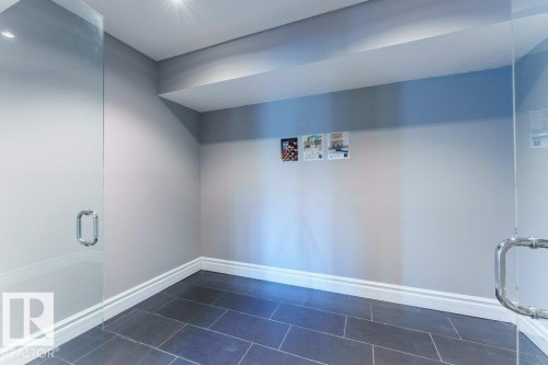 Spacious room featuring dark rectangular floor tiles, light gray walls with white baseboards, and a dropped ceiling with recessed lighting - 328 52327 Range Rd 233, Rural Strathcona County, AB 