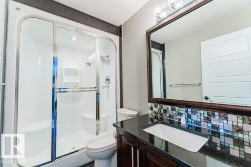 Three-piece bathroom featuring a glass-enclosed shower with integrated seating, a dark wood-finish vanity with a built-in sink, a speckled dark countertop, and a tiled backsplash - 328 52327 Range Rd 233, Rural Strathcona County, AB 