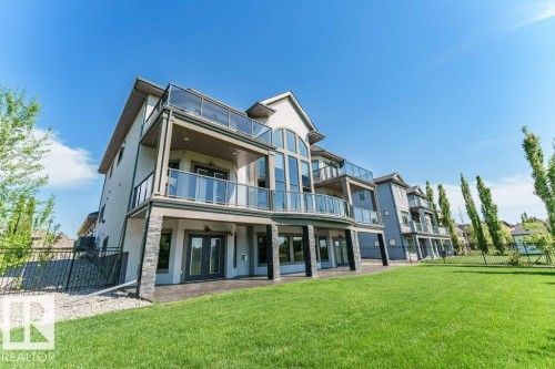 Expansive rear exterior featuring multiple balconies with glass railings, a ground-level patio, large arched windows, and stone accents - 328 52327 Range Rd 233, Rural Strathcona County, AB 