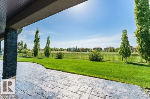 Stamped concrete patio with a stone-clad pillar, overlooking a spacious lawn and mature trees, bordered by a black metal fence - 328 52327 Range Rd 233, Rural Strathcona County, AB 