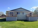 Rear facade featuring a light green textured exterior, two elevated wood decks with railings and blue-grey siding, multiple windows, and a dark shingled roof - 4537 50 Avenue, Cold Lake, AB 