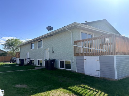 Exterior featuring light green textured stucco siding, a wooden deck with railing, gray horizontal vinyl siding on the lower level, a white exterior door, and multiple windows - 4537 50 Avenue, Cold Lake, AB 