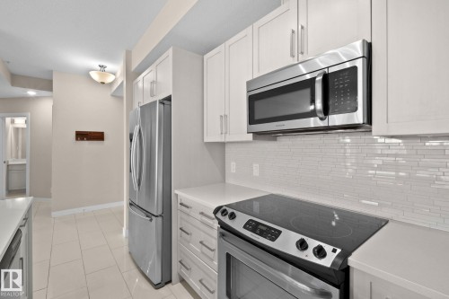 Modern kitchen featuring white shaker cabinetry, stainless steel appliances, a smooth-top range, white countertops, and a white subway tile backsplash - 309 625 Leger Way, Edmonton, AB 