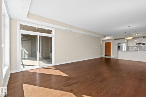 Open-concept living area featuring rich wood-finish flooring, a wall of windows, and sliding glass doors to an outdoor space - 309 625 Leger Way, Edmonton, AB 