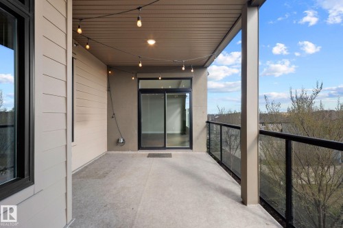 Spacious private balcony with concrete flooring, glass panel railing, and string lighting - 309 625 Leger Way, Edmonton, AB 
