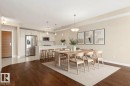 Open-concept living space featuring wood-finish flooring, a contemporary kitchen with stainless steel appliances, white cabinetry, and a central island with bar seating - 309 625 Leger Way, Edmonton, AB 