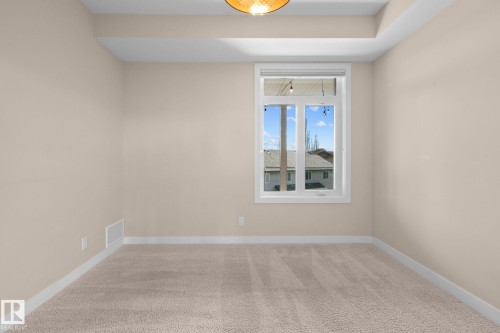 Carpeted room with a single pane window featuring white trim and a neutral wall color - 309 625 Leger Way, Edmonton, AB 